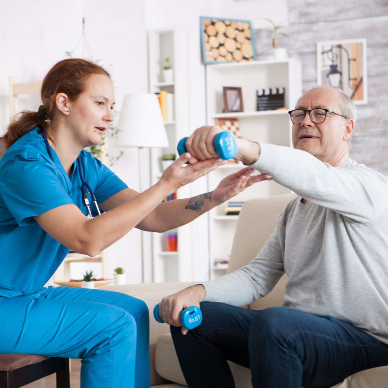 Senior man in nursing home with doing physical therapy with help from nurse using dumbbells.